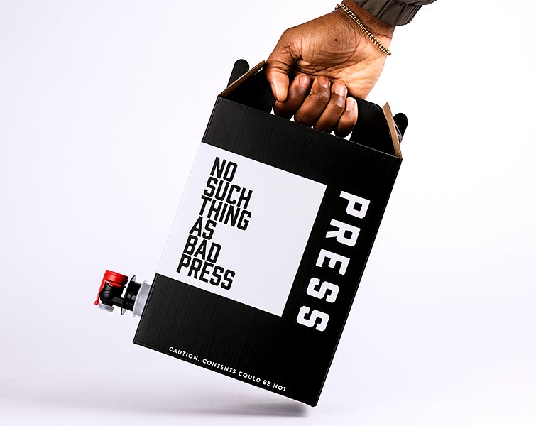 A hand holding a cup of iced tea with a straw, packaged in a black and white cardboard holder with text.