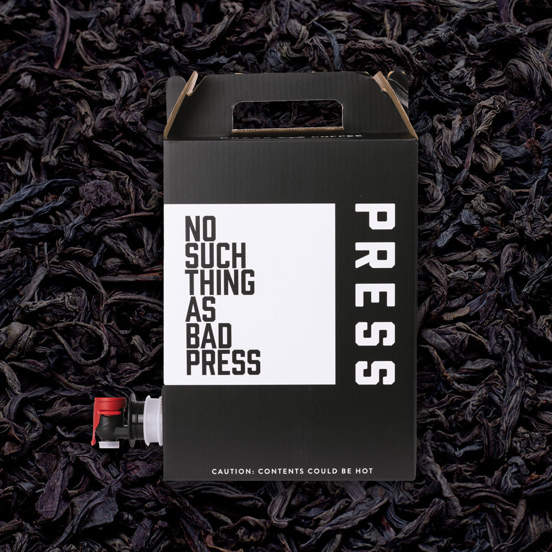 Black box with 'No Such Thing as Bad Press' text on a bed of dark tea leaves.